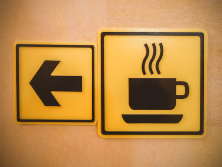 Two yellow square signs depicting arrow and cup hang on the wall.の写真素材