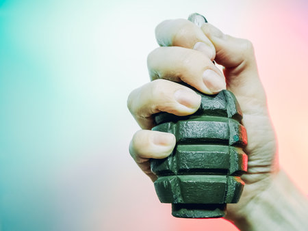 A closeup photo of a hand squeezes a green military grenade on a multicolor background.の写真素材