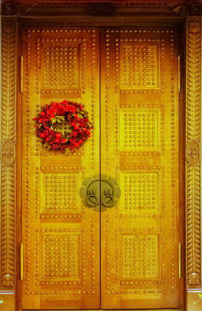 Wooden patterned doors of golden color with carved platbands and with a New Years wreath hanging on...