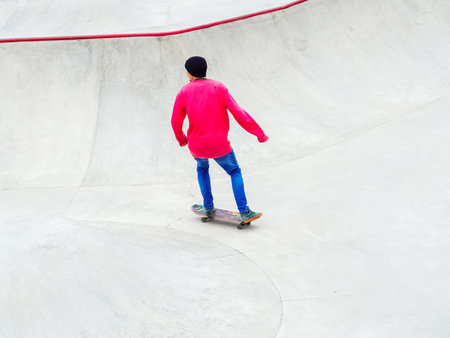 A guy in blue pants and a pink sweatshirt rides a skateboard in a skateparkの写真素材