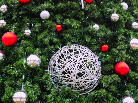 A silver wicker ball entwined with a garland hangs among the spruce branches, red and silver balls and a garland with blue small lightsの写真素材