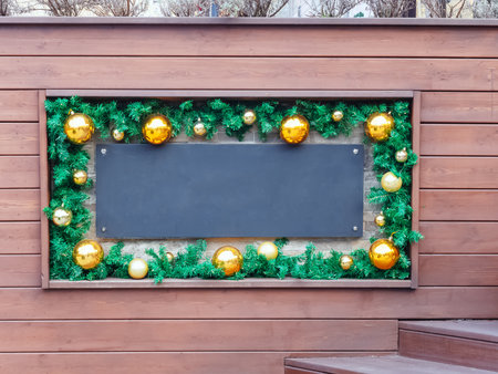 Blank black plaque in a frame with New Years decor in the form of fir branches and golden balls on the wall with wooden slatsの写真素材