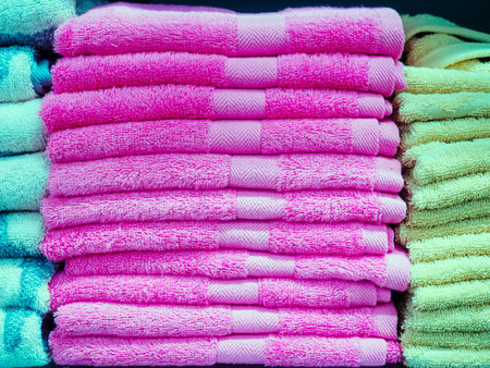 A stack of pink identical terry towels in the middle and turquoise and green towels on the sidesの写真素材
