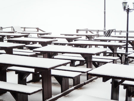 Wooden identical tables with benches covered with snow stand in a row on the terrace of a street cafeの写真素材