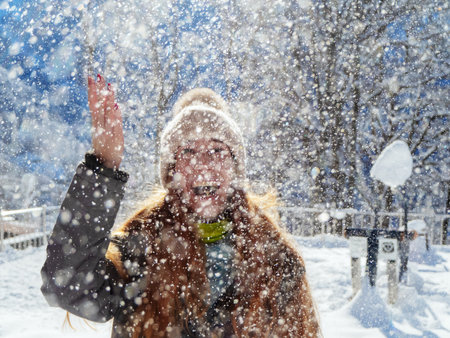 Snow falls from above on a joyful girl illuminated by the sunの写真素材