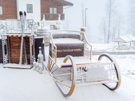 Russia, Sochi 22.01.2020. Decorative sleigh, skis and bottles of vodka strewn with snow stand in front of a building on snowy foggy dayのeditorial素材