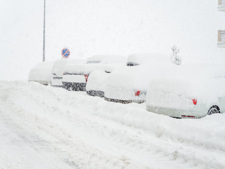 Snow-covered road with cars parked along it covered with snow during winter cold and blizzardの写真素材