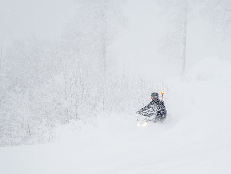 A man on a snowmobile rides through snowdrifts in heavy snow and fog