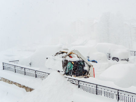 Snow plow tractor and other vehicles heavily covered with snow in a parking lot during a snowstormの写真素材