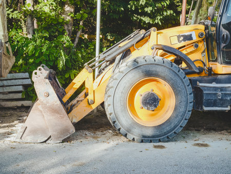 Front of a yellow bulldozer with a wheel and a ladle on a background of green vegetation on a...
