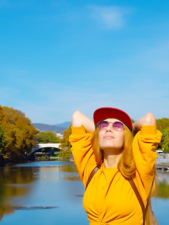 Girl in sunglasses turns her face to the sun against the background of the river and sky