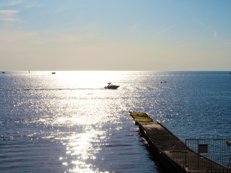 Sea with shining sun glare pier and boats under blue skyの写真素材