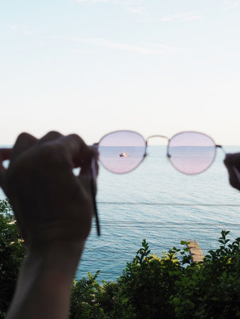 View through sunglasses a boat floating in the distance into the seaの写真素材