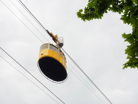 Yellow retro lift on a cable against the background of a cloudy sky and branches with green leavesの写真素材