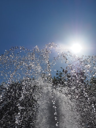 The jets of the fountain spouting upward with drops shining in the sun against the background and cloudless skyの写真素材