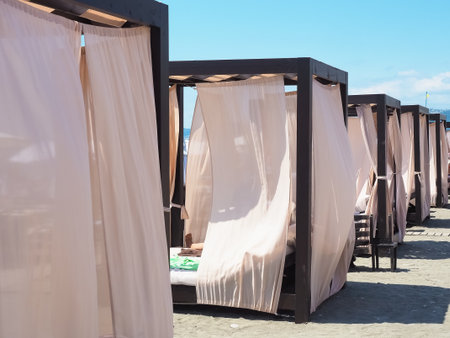 Beach cabins with a metal frame and light curtains stand in a row on the sand on a sunny summer dayの写真素材