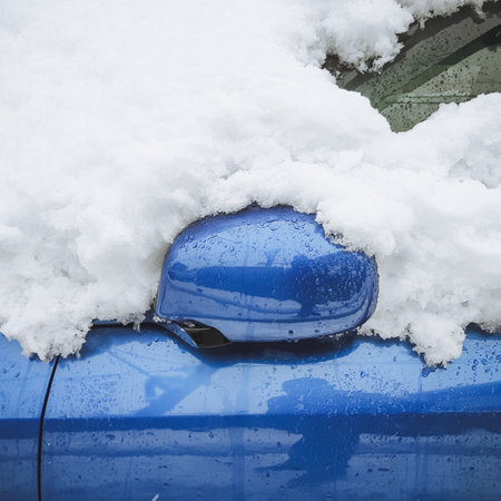 A fragment of a wet blue car covered with snow with a folded rear-view mirror. Closeup photoの写真素材