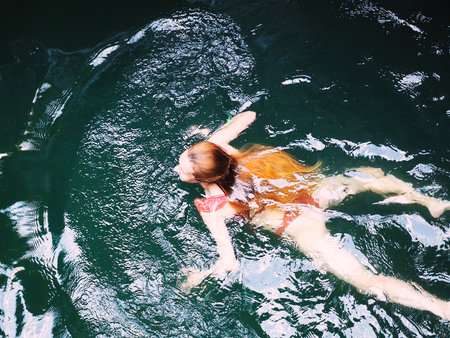 Long-haired girl in an orange bikini swims in a dark turquoise riverの写真素材