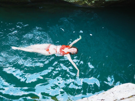 Girl in an orange bikini swims on her back in a turquoise riverの写真素材