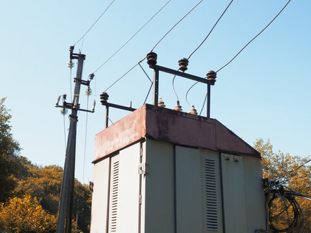 Top of a transformer booth with power lines against a background of blue sky and trees