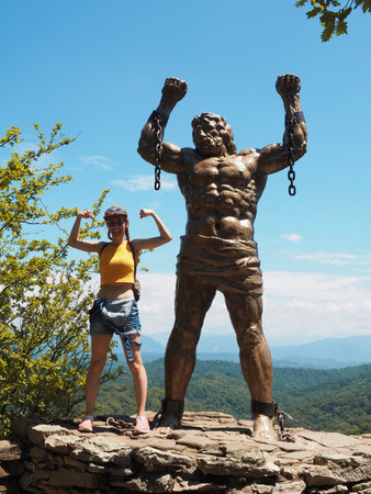 Russia, Sochi 12.07.2020. Smiling girl posing near the tall statue of prometheus on the background of a mountain valley on a sunny summer dayのeditorial素材