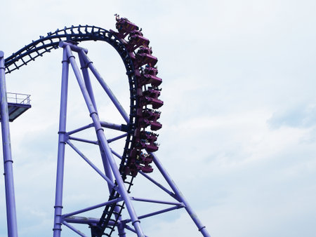 Russia, Sochi 16.04.2021. Fragment of lilac attraction roller coaster with people riding on it against the cloud skyのeditorial素材
