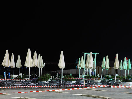 Night empty beach with sun loungers and folded umbrellas fenced off with a barrier tapeの写真素材