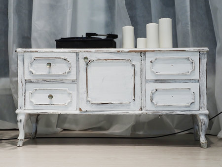 A white retro commode with a music player and candles standing on it. Interior decor