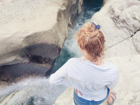 A girl standing on the edge of the canyon looks into the stormy stream of the river flowing in a narrow gorgeの写真素材