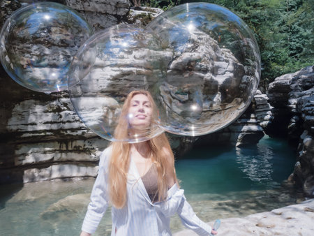 A girl peers through a triple stuck together flying soap bubble against the backdrop of canyons and a turquoise riverの写真素材