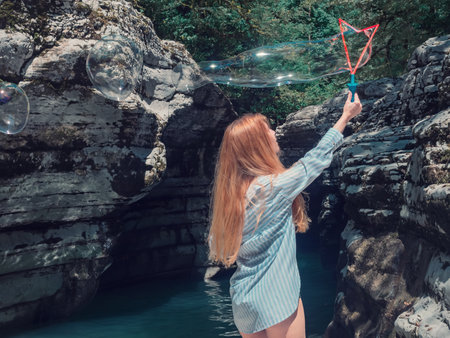 Redhaired girl blows big soap bubbles in the canyon gorge by the waterの写真素材