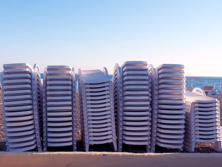 Beach white sun loungers stacked on top of each other stand in a row on the seashore under the blue skyの写真素材