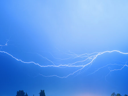 A branching bolt of lightning sparkles in a bright blue skyの写真素材