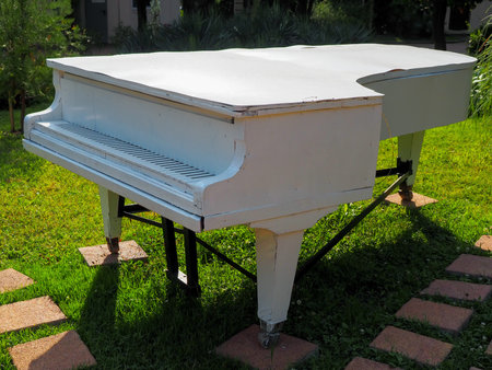 An old white wooden grand piano stands on a green lawn in the park. Park decorの写真素材