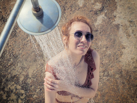 The girl in sunglasses and a bikini washes under the shower outdoors. Beach shower