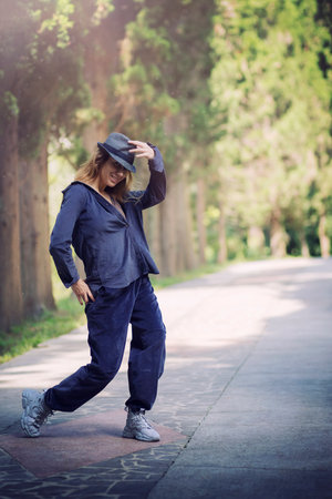 Smiling girl in blue clothes and a hat in a dancing pose in a park alleyの写真素材
