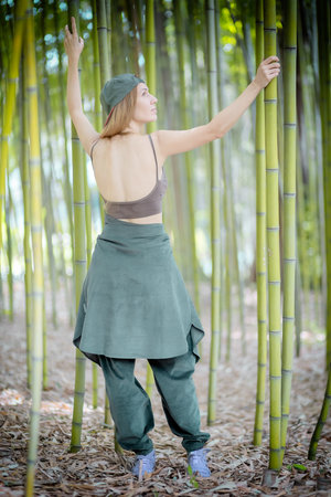 Hip-hop girl in a tank top with an open back stands in a bamboo grove holding green trunksの写真素材