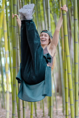 Laughing hip-hop girl hung with her legs lifted up on green trunks in a bamboo groveの写真素材