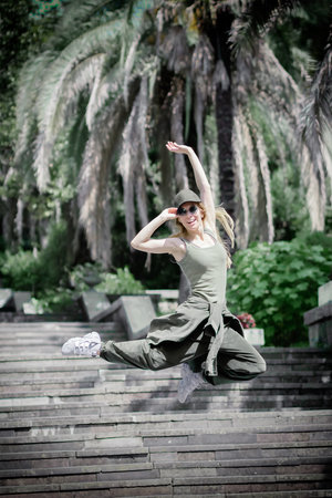 Cheerful girl in hip-hop outfit hovers in a high jump against the background of steps and palm trees in south parkの写真素材