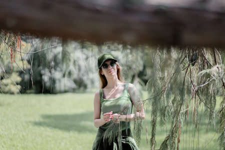 A girl in a sports green outfit is standing on a summer lawn. View through the branches of a treeの写真素材