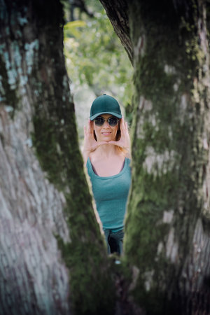 Between the forked trunks of a tree, a girl leaning her palms to her faceの写真素材