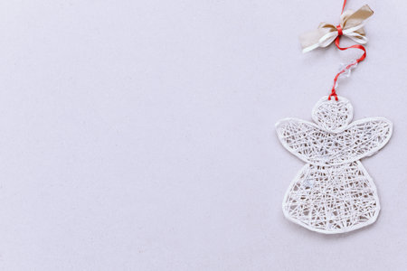 White handmade angel on a red ribbon with a bow on the right on a light blank background. Christmas...