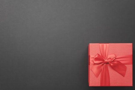 Red gift box with a bow in the corner on a dark gray background. Top view. greeting card