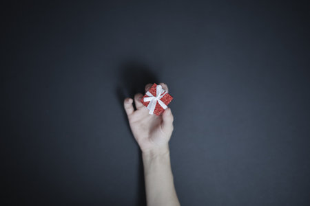 Womens fingers are holding a tiny red shiny box with a white bow. Top view. Holiday giftの写真素材