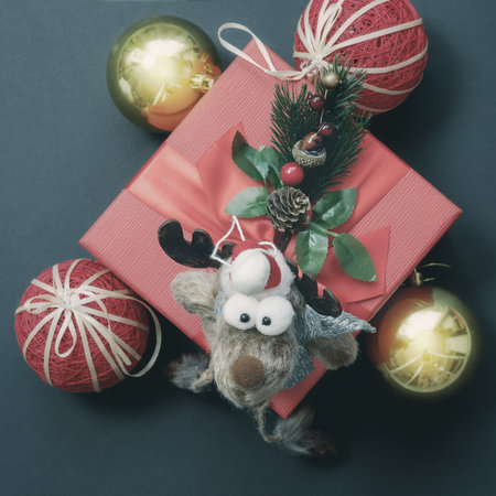 A funny toy goggle-eyed deer sits on a red gift box with Christmas balls and a coniferous twig. Christmas decorの写真素材