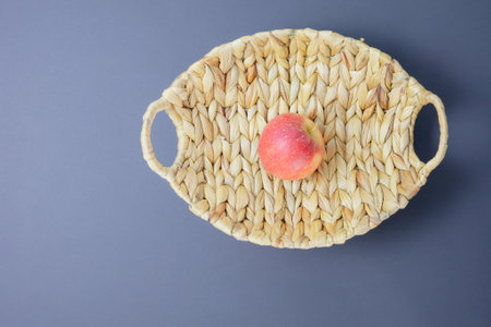 Beautiful wicker vase with one red apple on a matte gray background. Top viewの写真素材