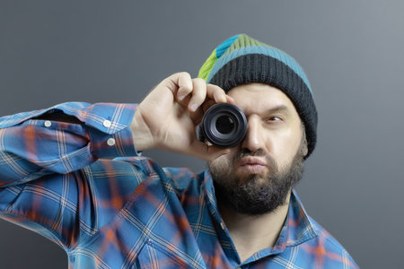 A bearded man in a striped hat with a funny grimace looks through a round lens