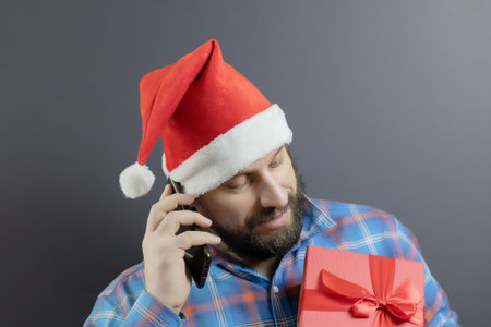 A man in a santa hat with a red box with a gift talking on a cell phoneの写真素材