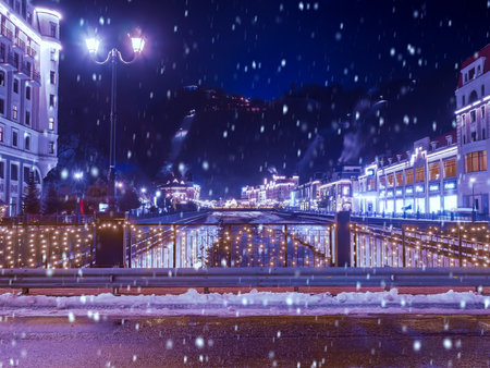 Russia. Sochi. Rosa Khutor 24.01. 2021. Winter Christmas atmosphere of the town. View from the bridge of the buildings illuminated by lamps and garlands in the winter, snowy evening.のeditorial素材