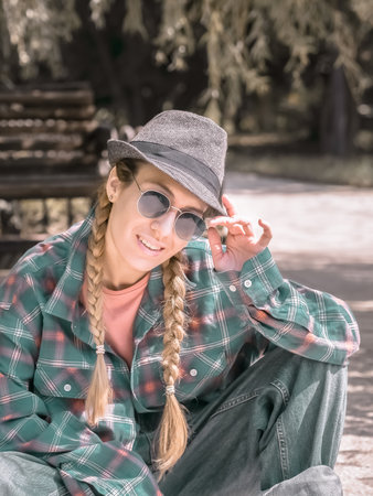 Smiling lady with two pigtails wearing hat and plaid shirt in sunlit park